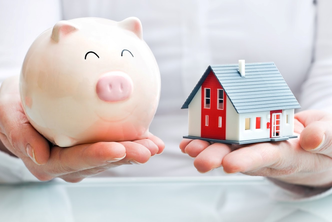 Image of a person holding a piggy bank and a small house in his hands.