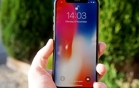 iPhone X displaying a multicolor lock screen held up by a hand.