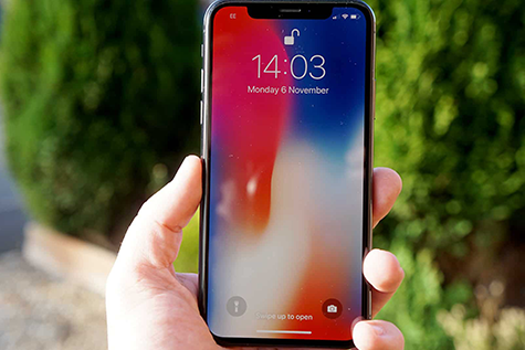 iPhone X displaying a multicolor lock screen held up by a hand.