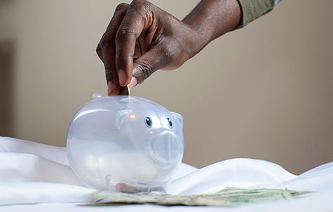 Clear piggy bank with hand putting coins in