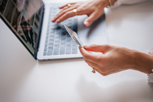 Caucasian woman's hands with rings, holding a credit card in one hand and entering numbers into the computer with the other 