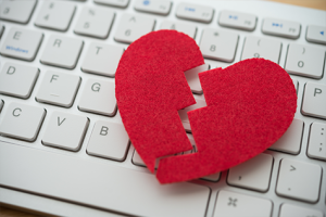 Red felt "broken" heart laying on a white computer keyboard