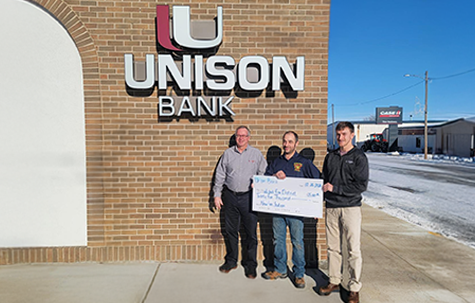 3 men standing in front of Unison Bank - Wishek - with a large check showing the donation to the Wishek Fire Department.