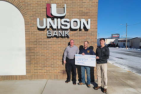 3 men standing in front of Unison Bank - Wishek - with a large check showing the donation to the Wishek Fire Department.