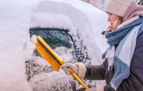 Girl bundled up in snow gear removing snow from her vehicle.