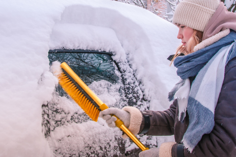 Girl bundled up in snow gear removing snow from her vehicle.